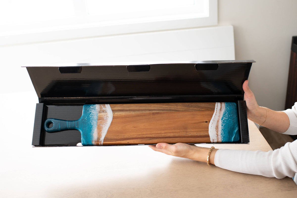 Person opening a black drawer to reveal a wooden tool with blue handle on a light-colored surface.