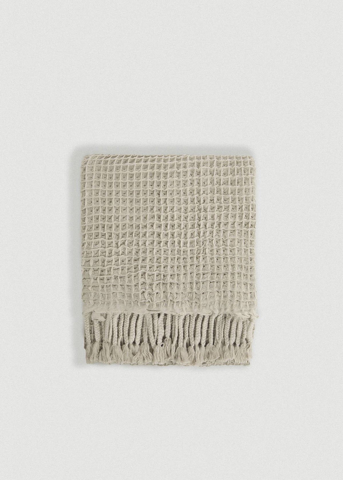 A light beige textured waffle-knit scarf with fringed edges, laid flat against a neutral light gray background.