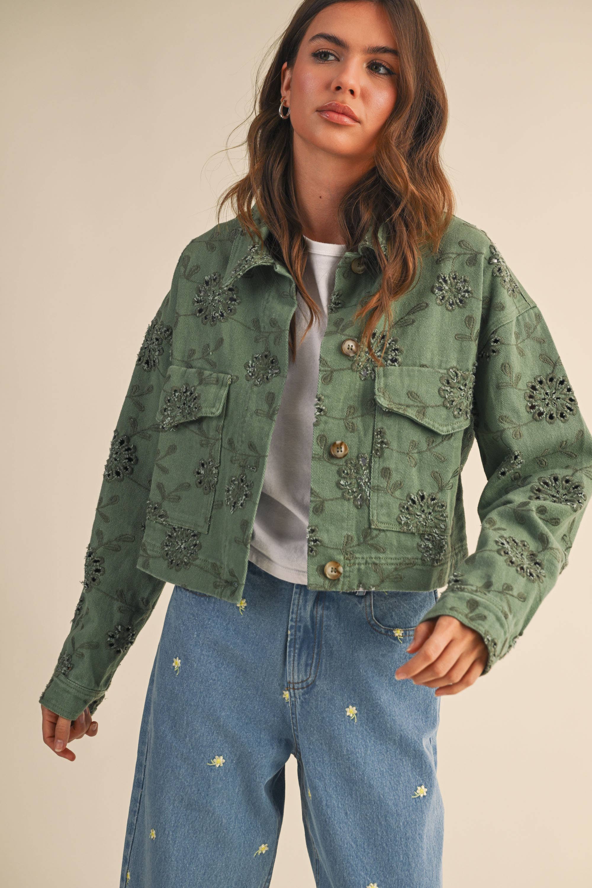 Woman wearing a green embroidered jacket and blue jeans on a beige background