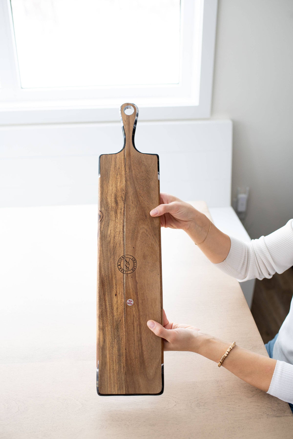 Person holding a wooden cutting board with a logo on a white surface