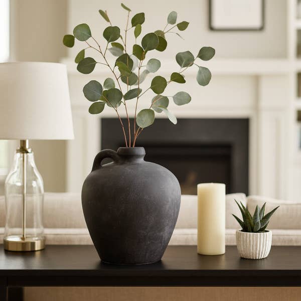 Decorative vase with greenery on a table in a living room setting.