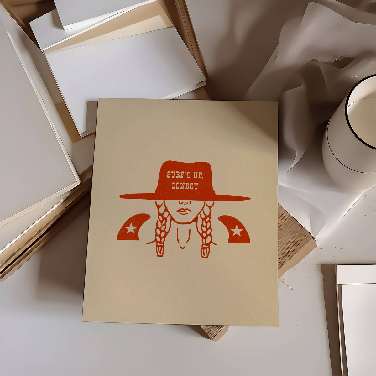 Notebook with a red illustration of a person wearing a cowboy hat and the text 'SHE'S UP, COWBOY' on a light surface.