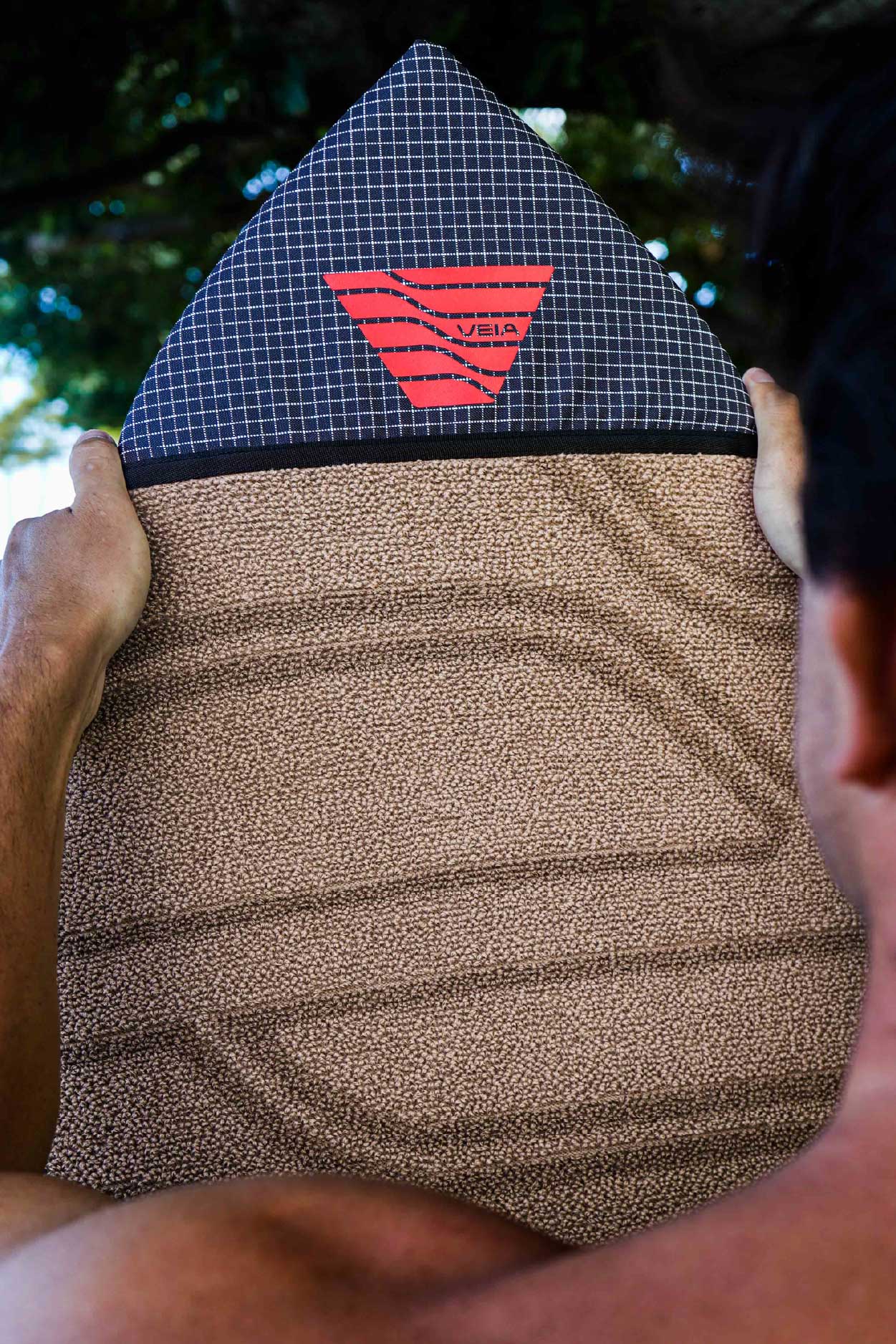 Person holding a textured brown and blue bag with a red logo.