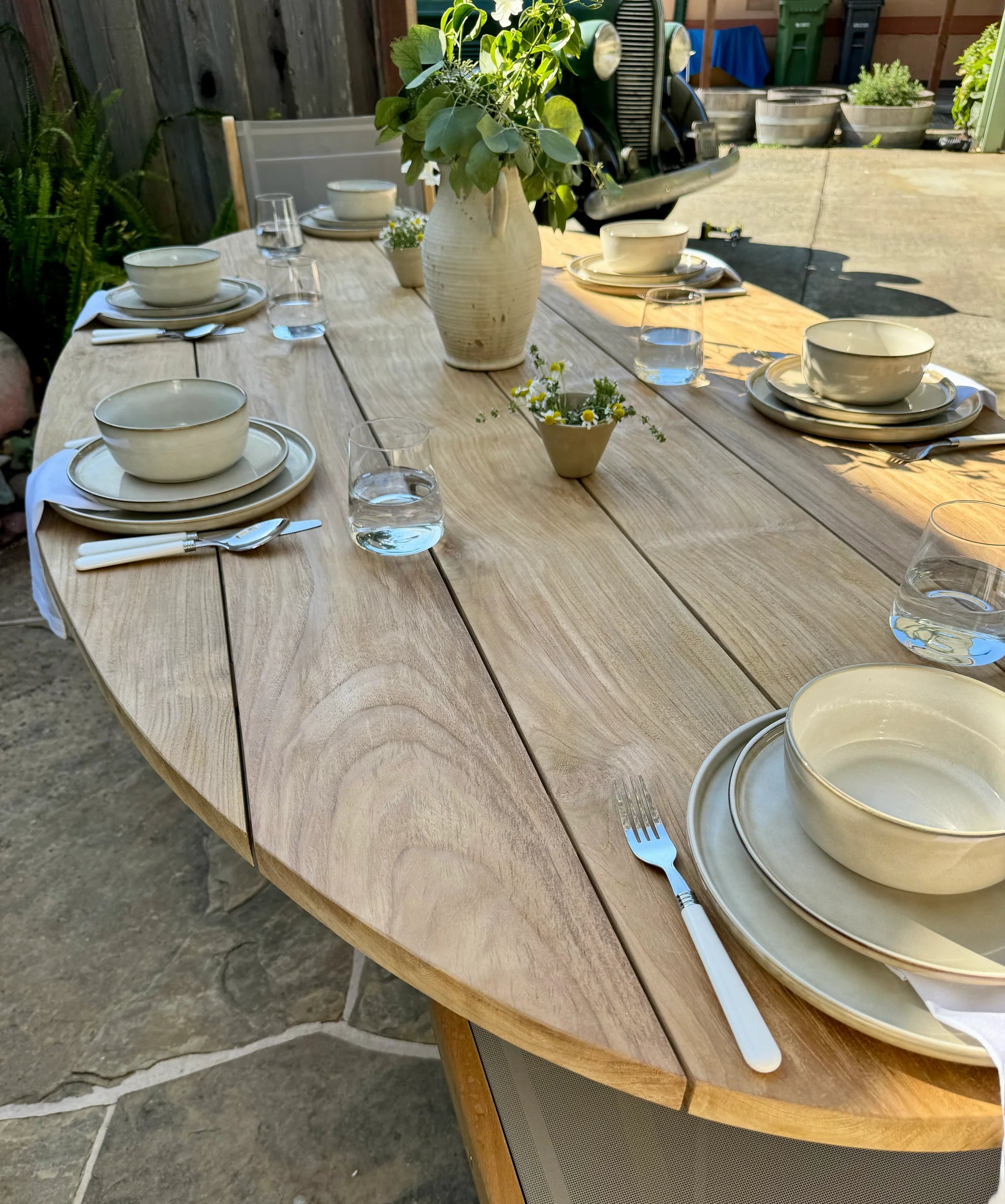 Dining table set with plates, bowls, and cutlery on a wooden table outdoors.