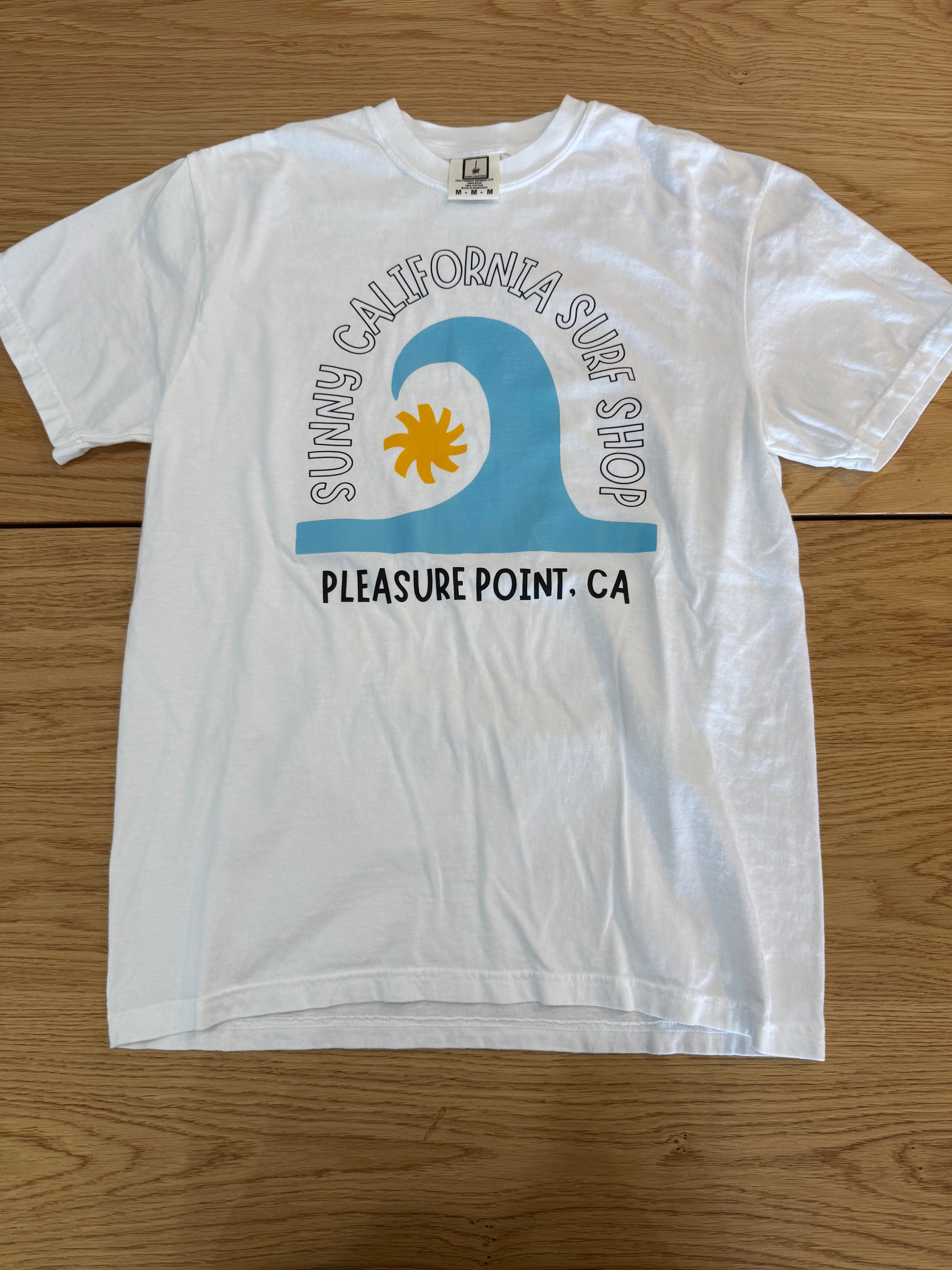White t-shirt with a blue wave and sun graphic on a wooden surface