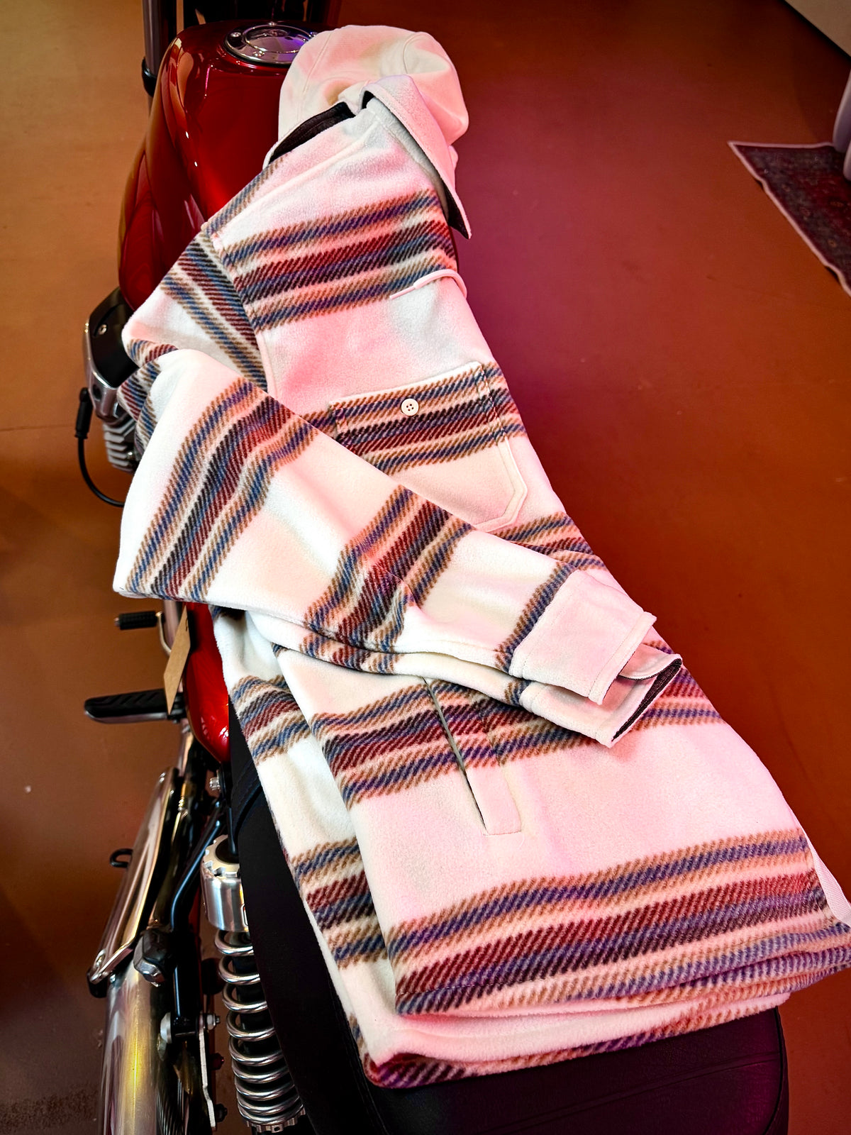 A folded pink and white Long Barn Hooded Fleece Shirt, draped over the seat of a red motorcycle.