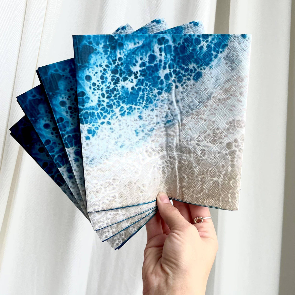 Hand holding a stack of blue and white patterned cards against a white curtain background