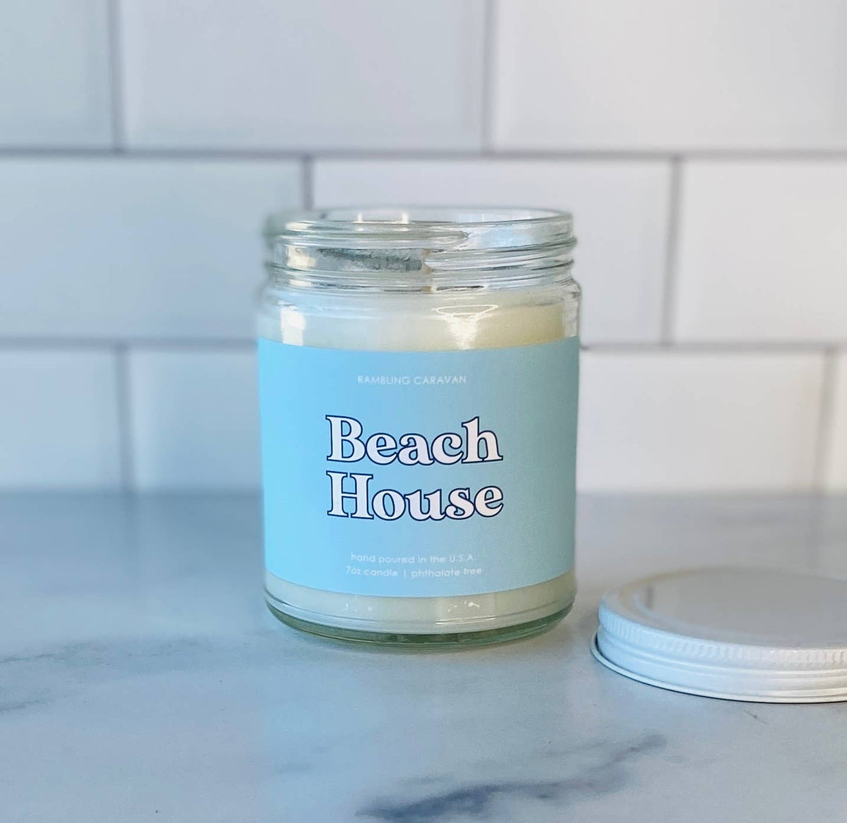 Candle jar labeled 'Beach House' on a marble surface with a tiled wall background