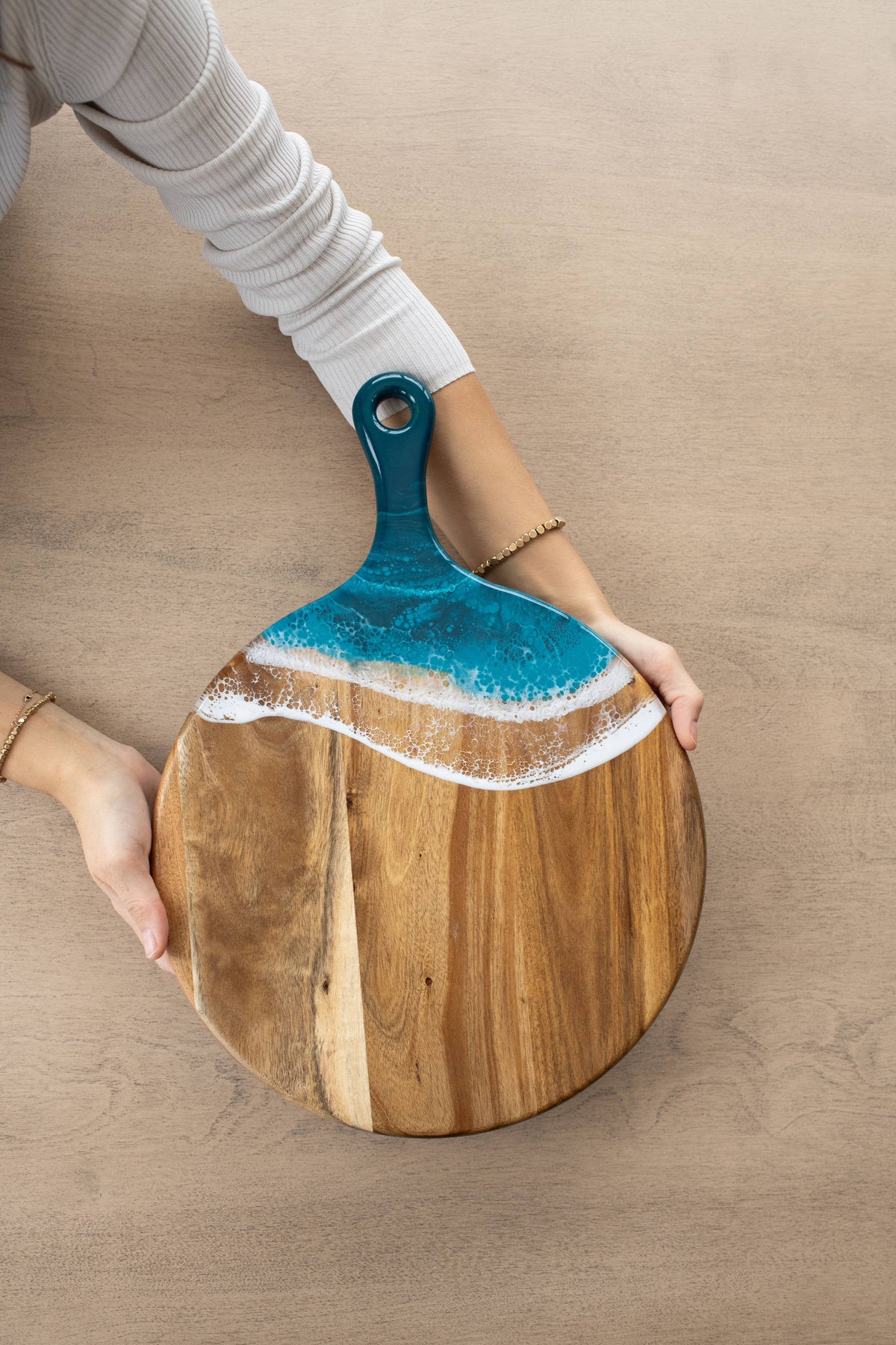 Wooden cutting board with a blue resin handle held by a person on a wooden surface