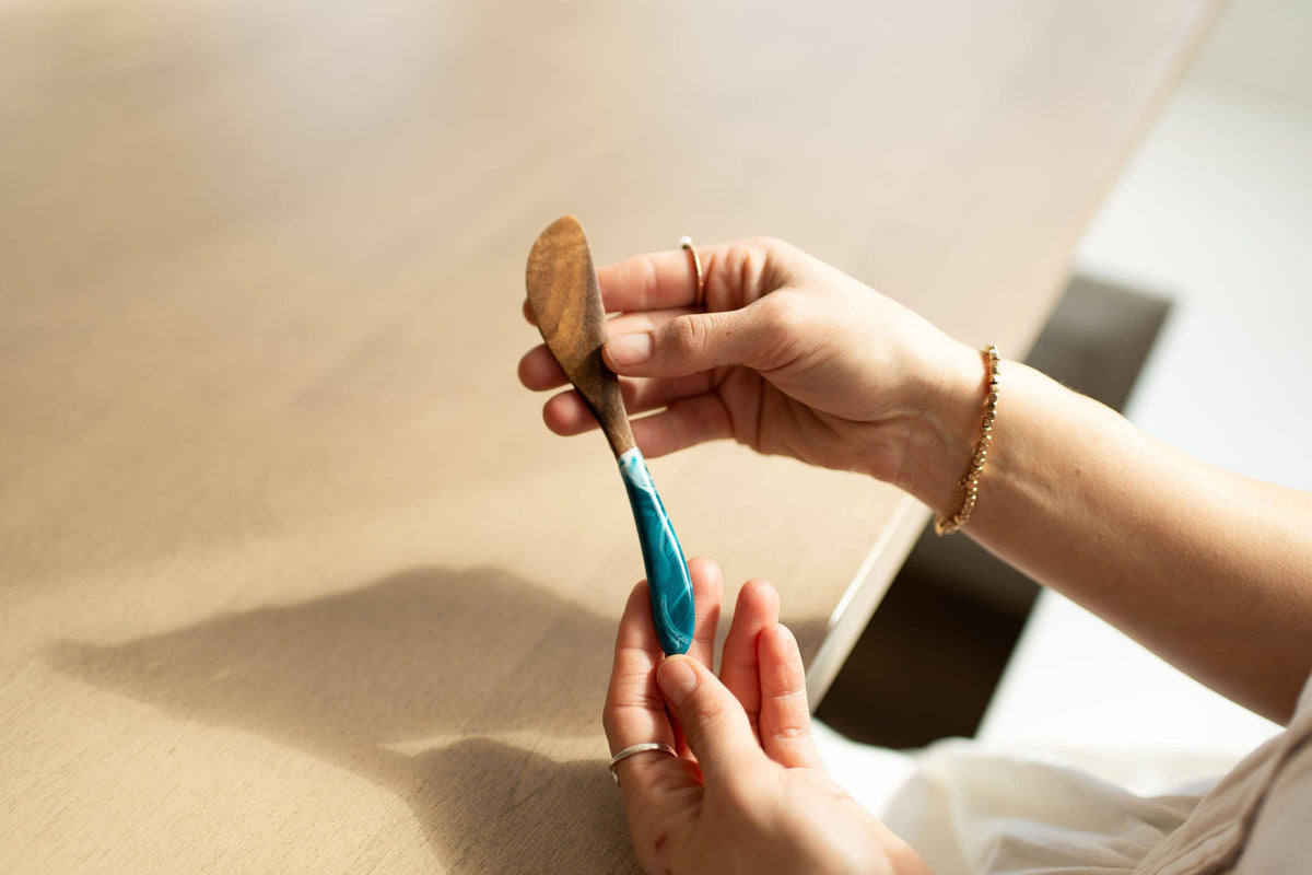 Person holding a small wooden object with a blue handle against a neutral background
