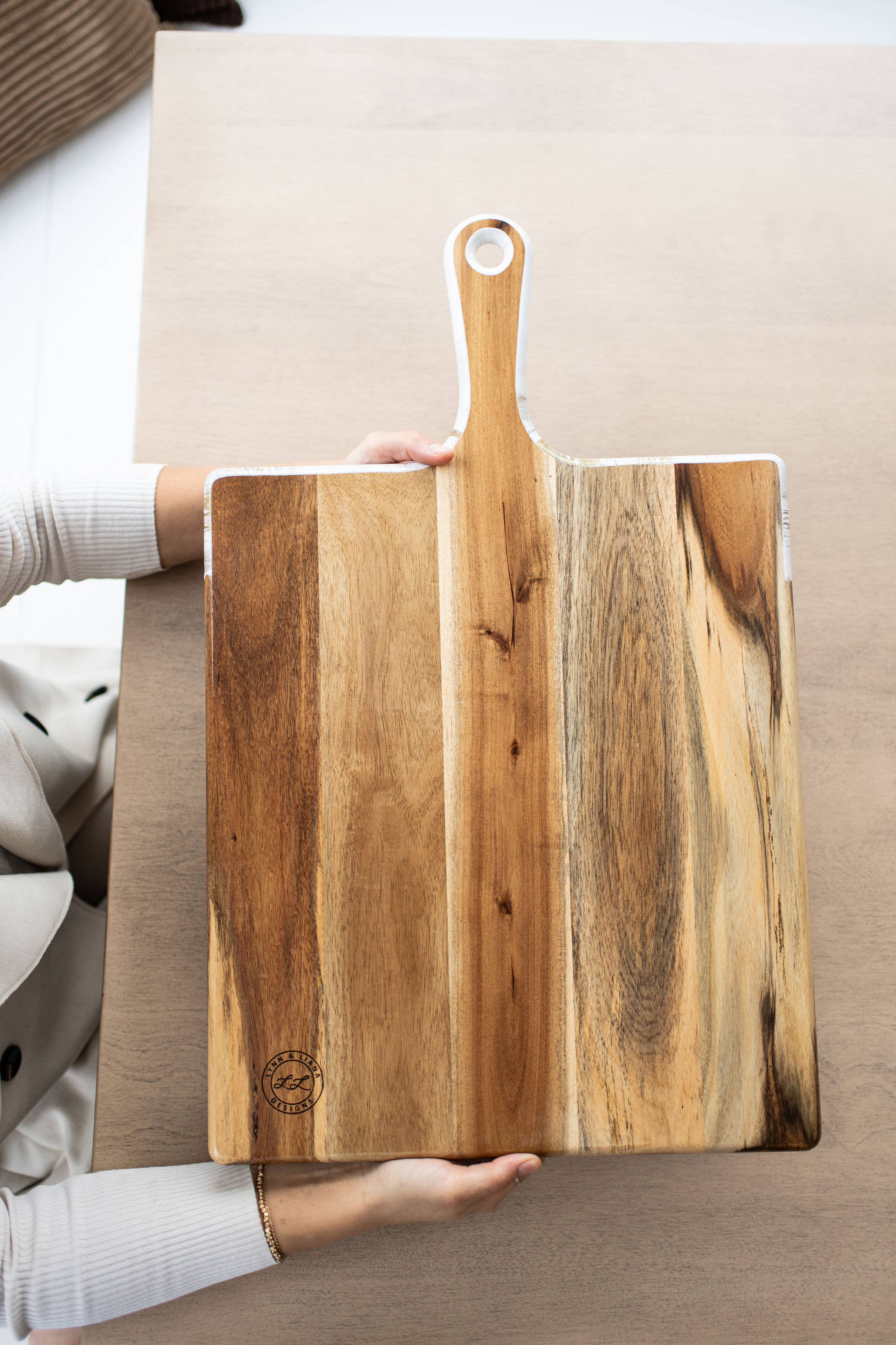 Person holding a wooden cutting board with a handle on a neutral background