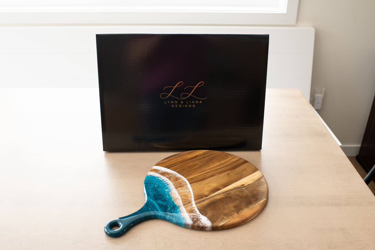 Wooden paddle with blue handle on a beige surface, with a black box in the background.