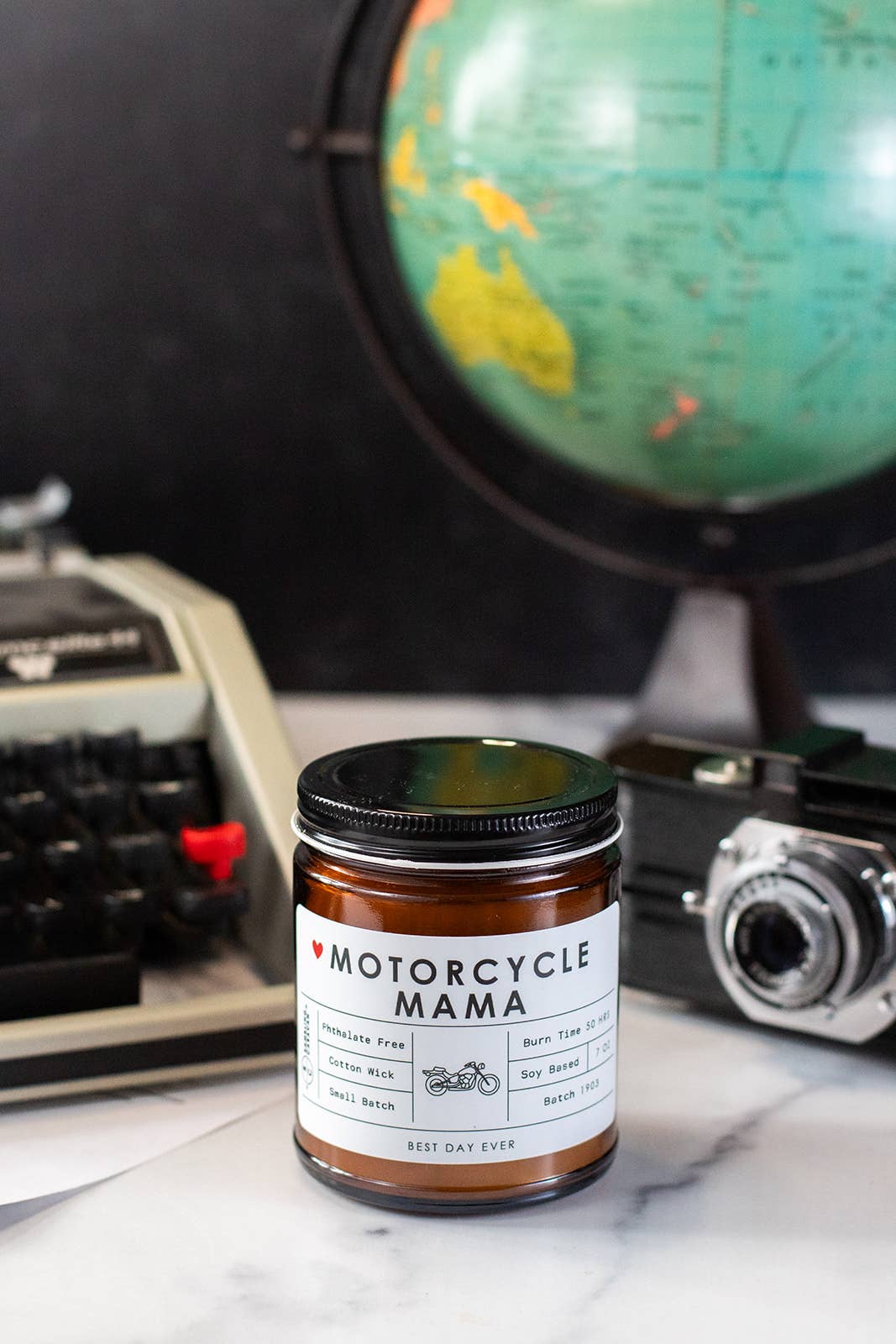 Jar labeled 'Motorcycle Mama' with a globe, typewriter, and camera in the background