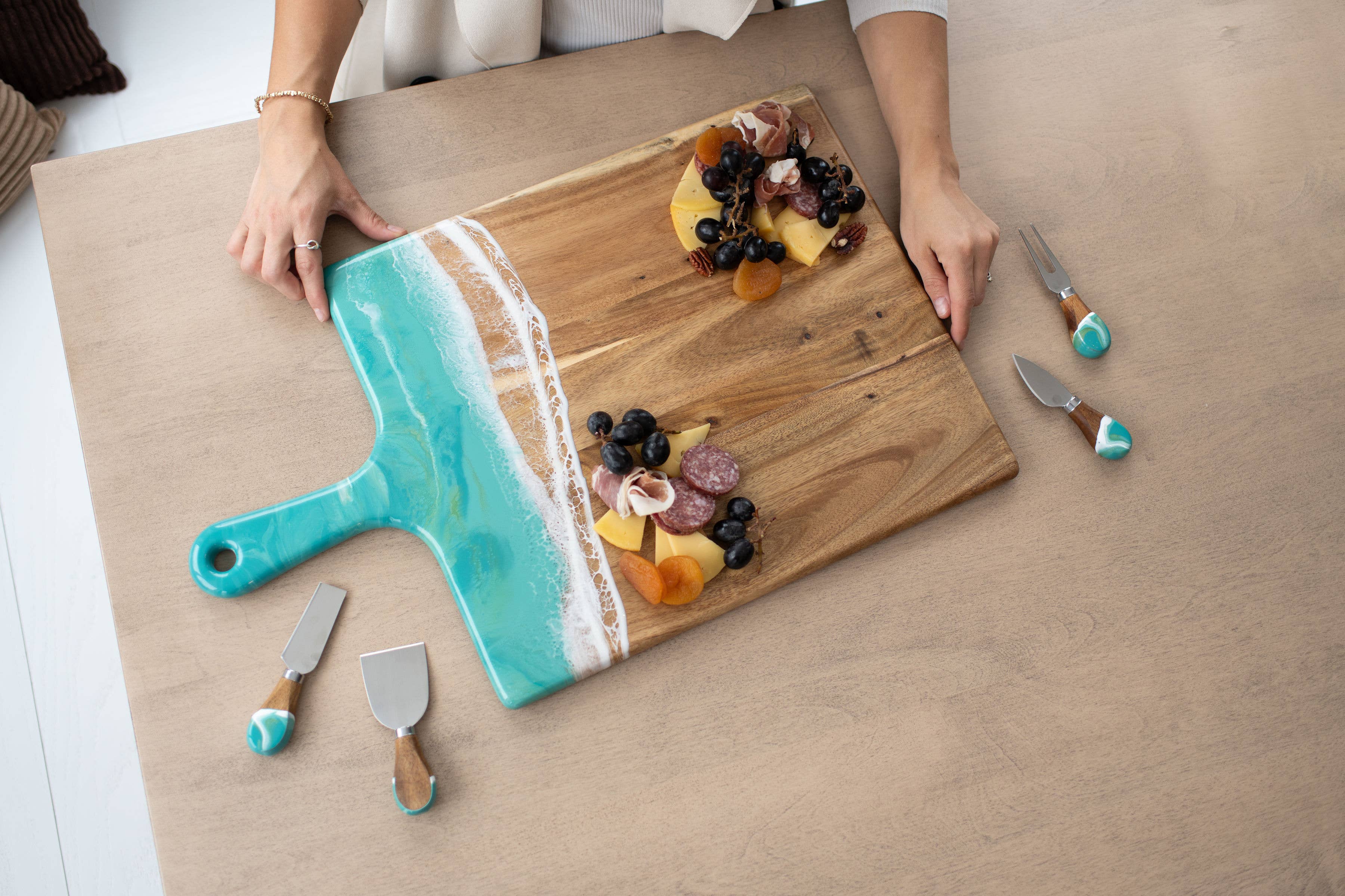 Wooden cutting board with decorative handle on a table with food and utensils.