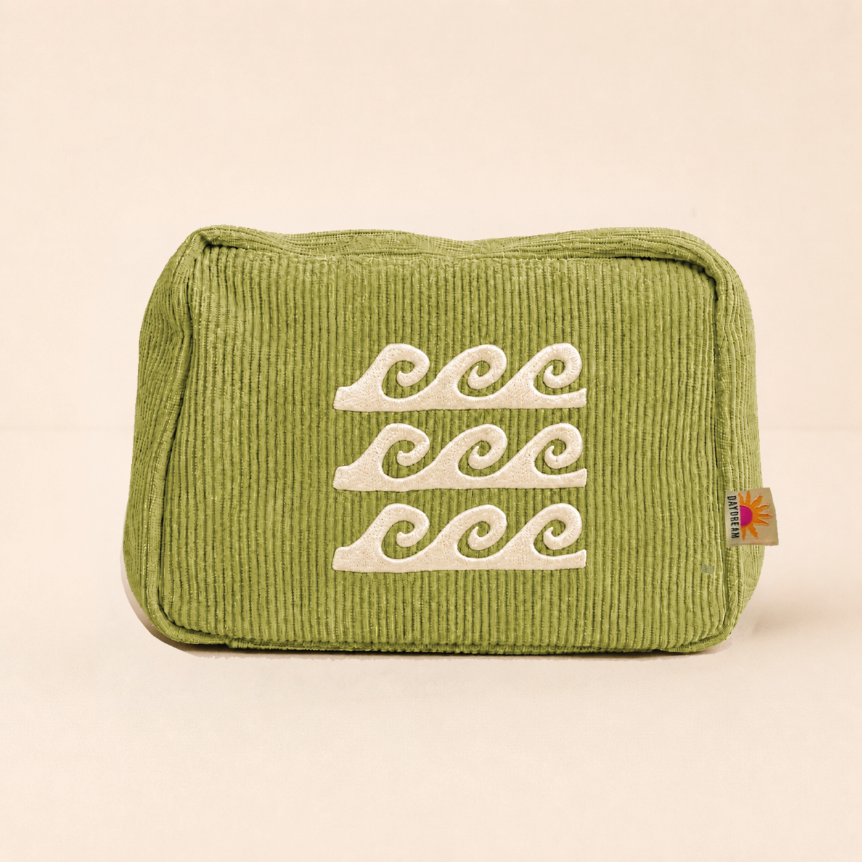 An olive green corduroy cosmetic pouch with three white embroidered wave motifs on the front, set against a solid light beige background.
