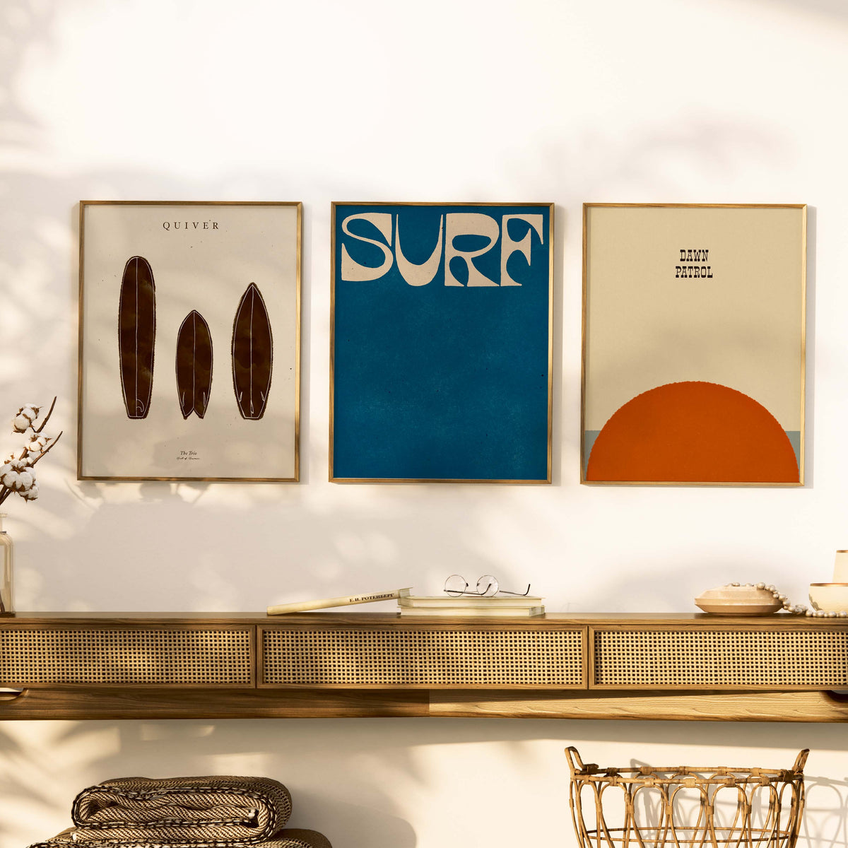 Three framed artworks on a wall above a wooden shelf with decorative items.