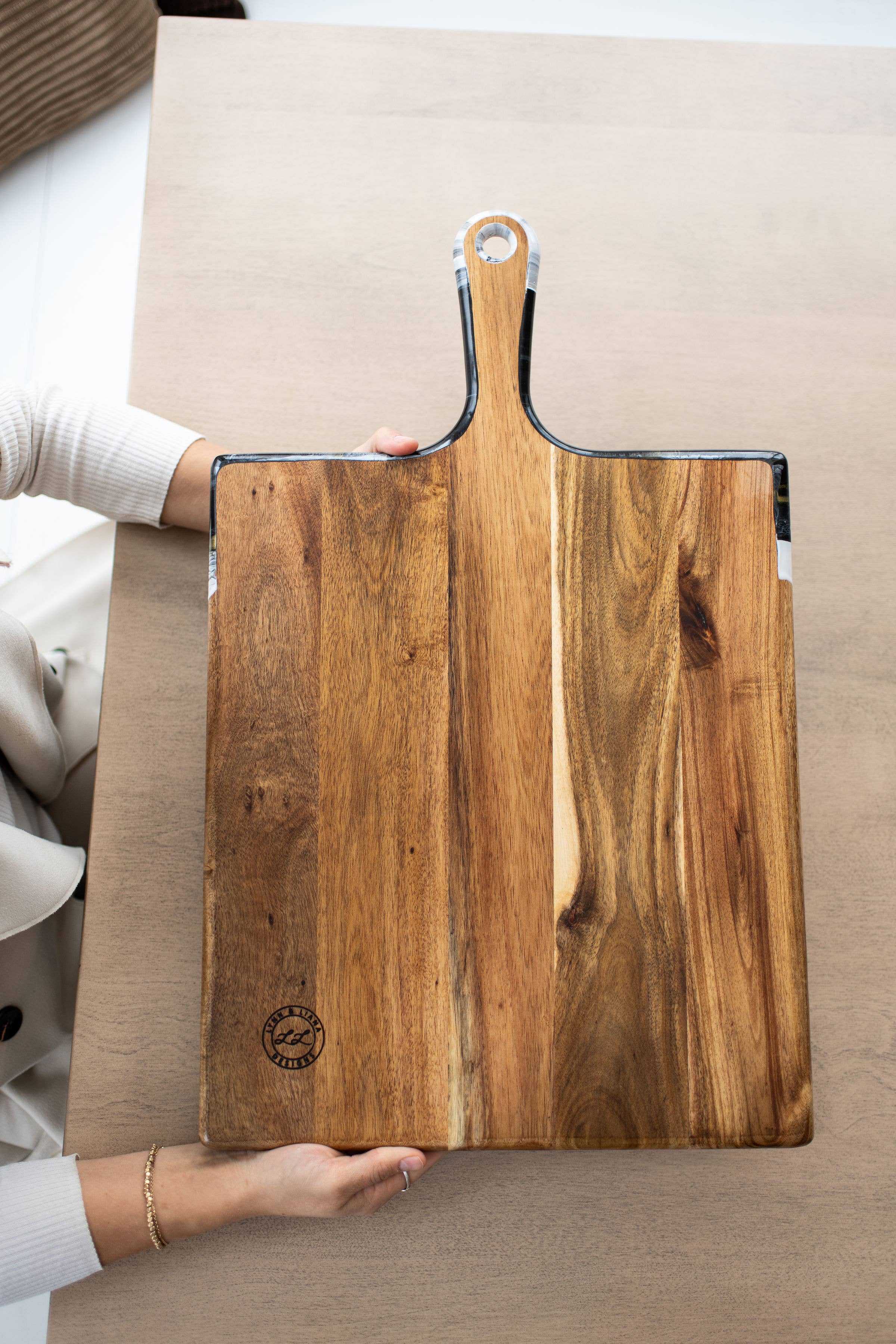 Wooden cutting board with handles held by a person on a neutral background