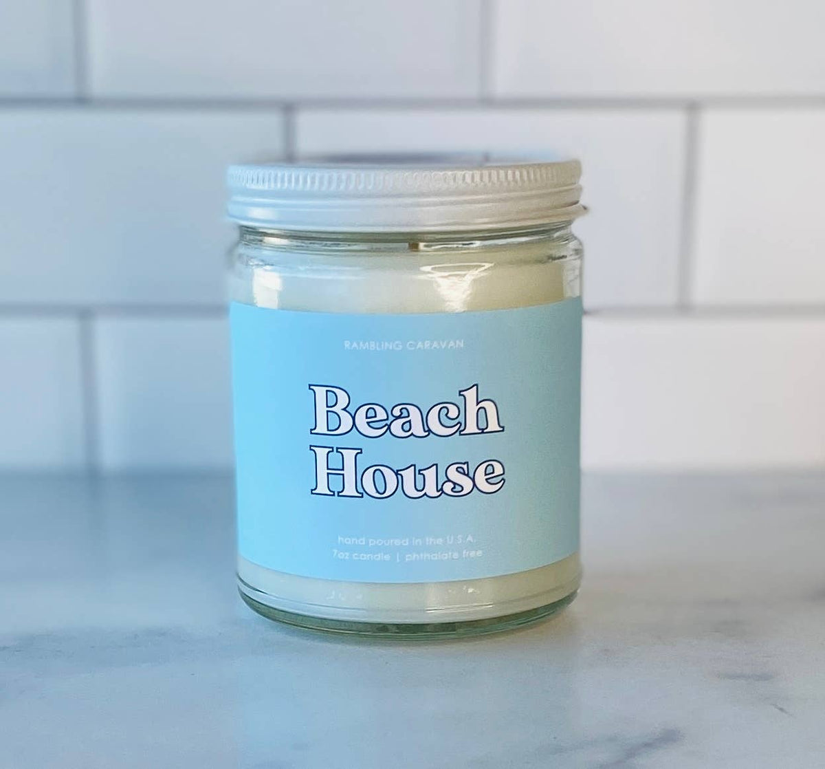 Candle jar labeled 'Beach House' on a marble surface with a tiled wall background