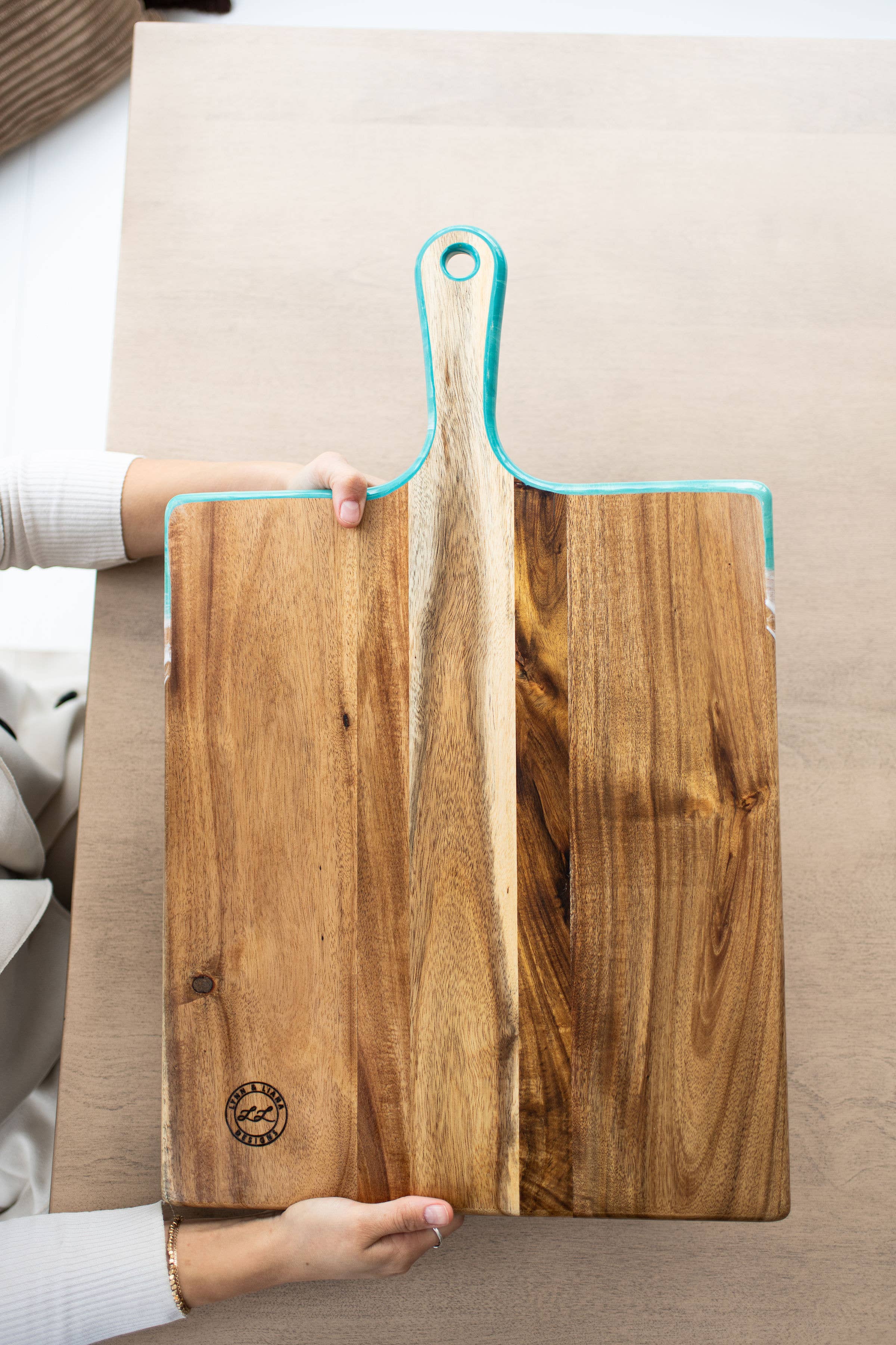Wooden cutting board with a blue handle held by a person on a neutral background