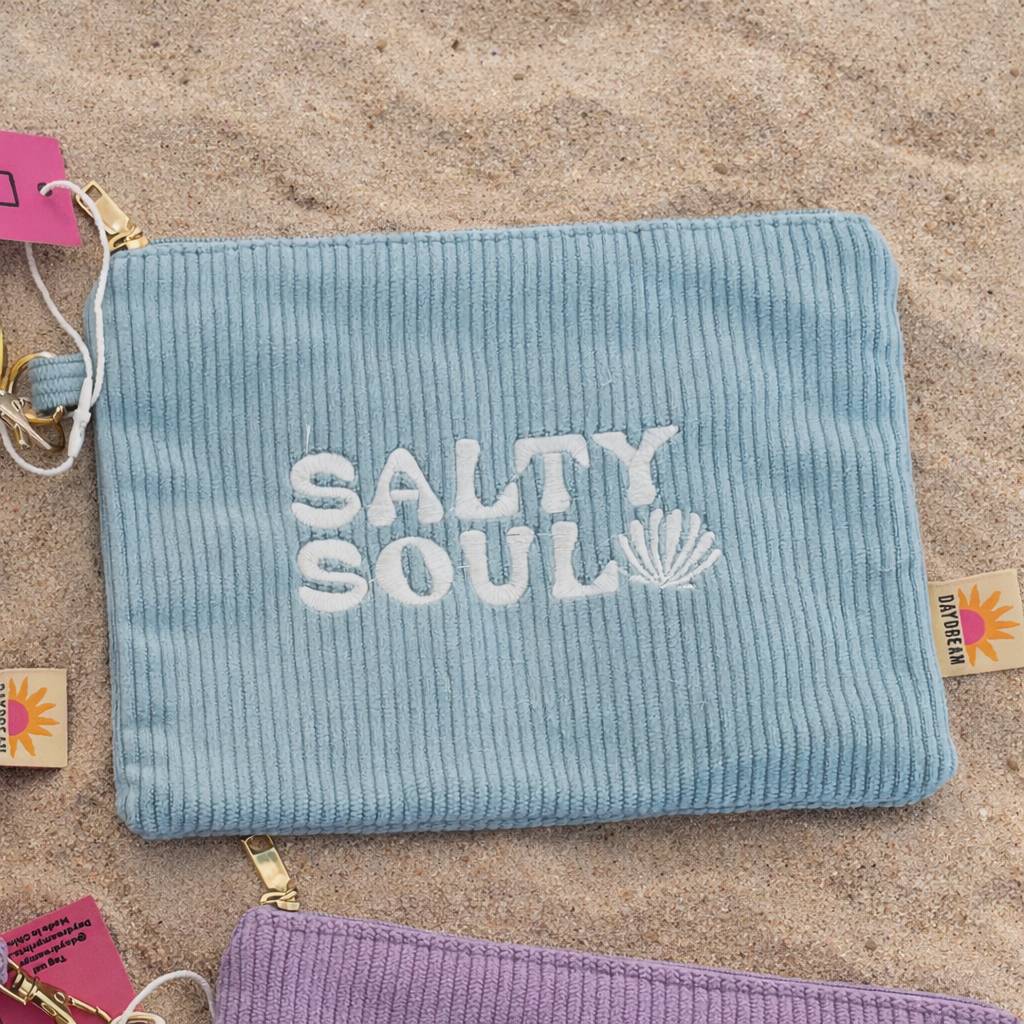 Blue corduroy pouch with 'Salty Soul' embroidery on a sandy background