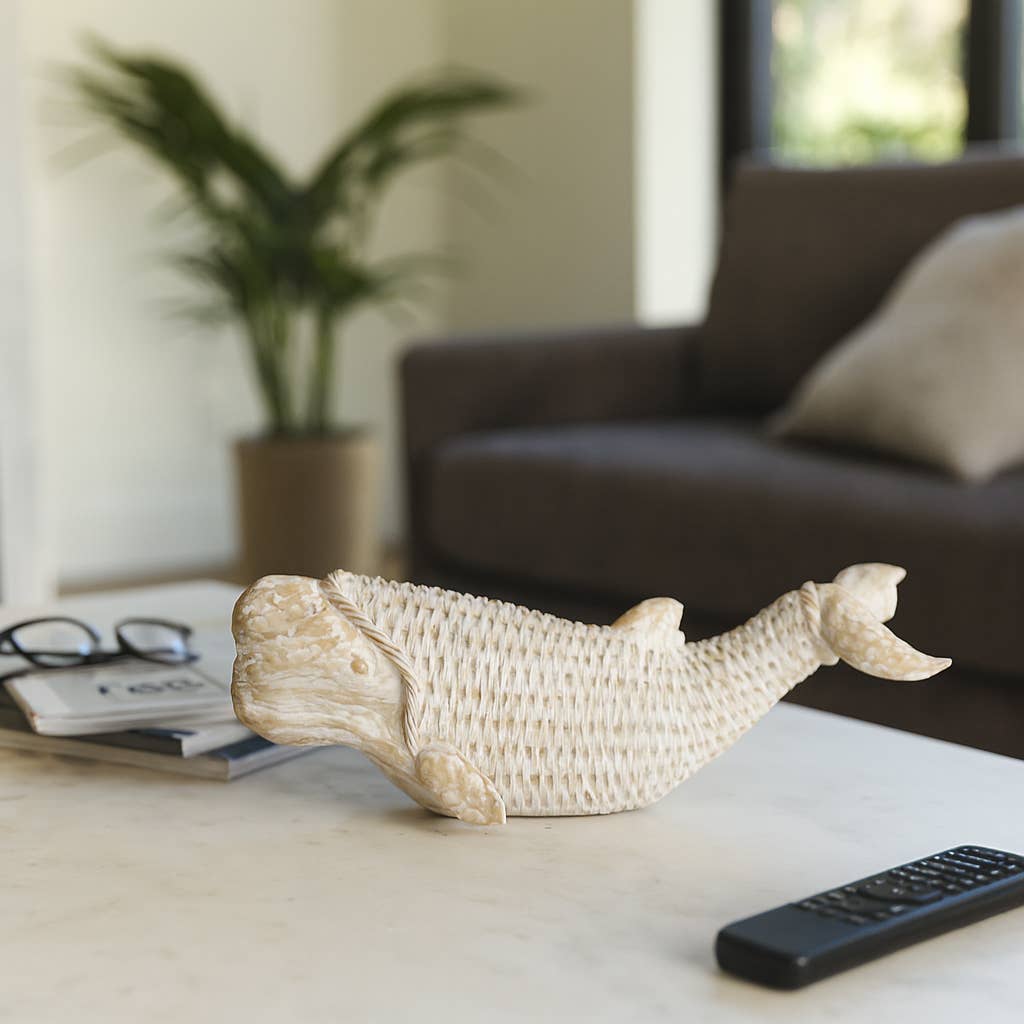A decorative carved whale figurine in a textured cream finish, displayed on a light marble coffee table in a modern living room setting.
