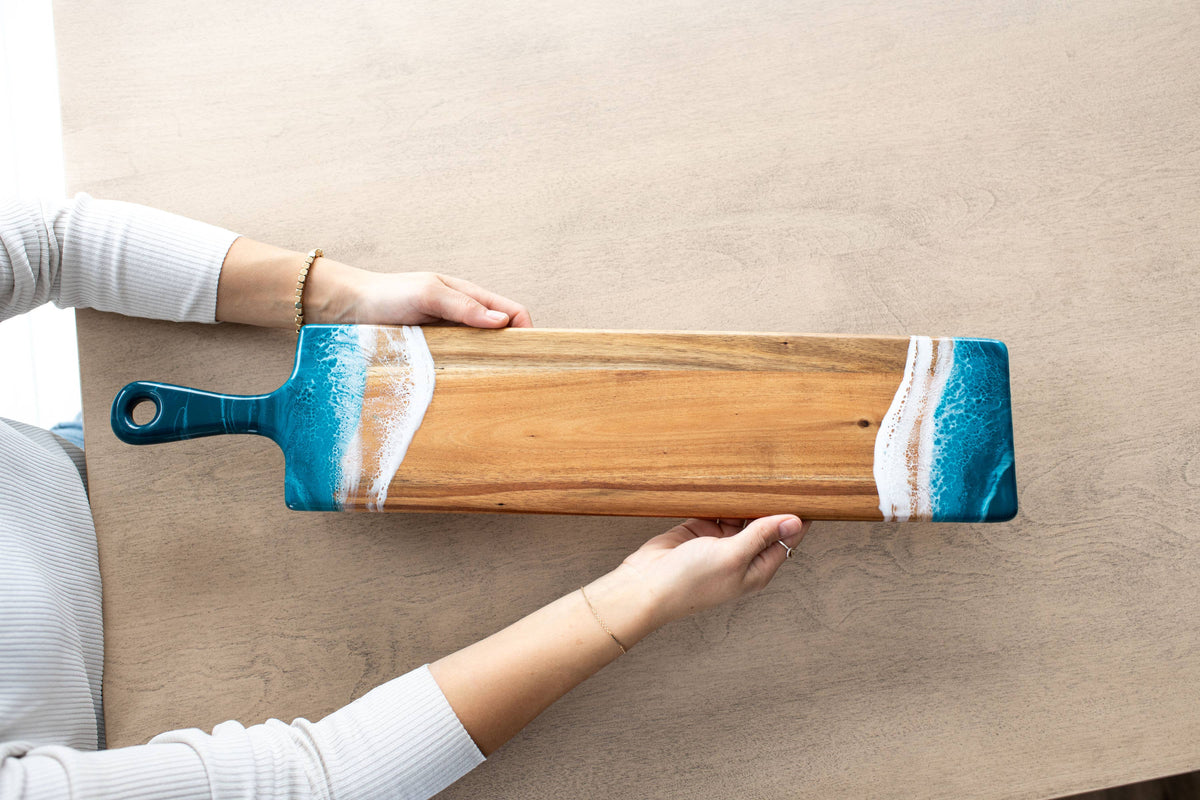 Person holding a long wooden paddle with blue and white design on a beige surface