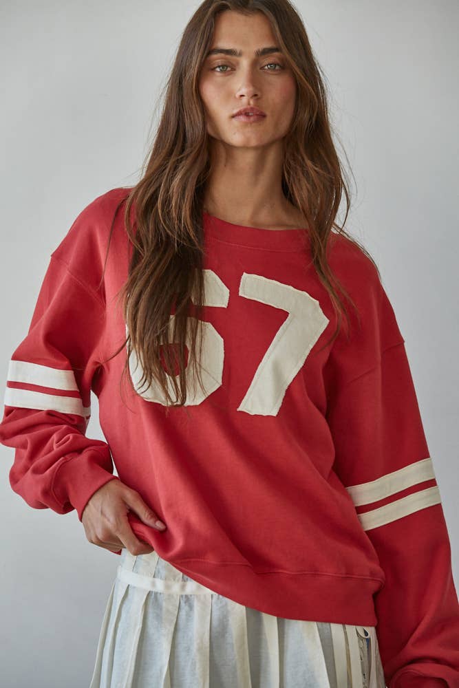 Woman wearing a red sweatshirt with the number 67 on a plain background