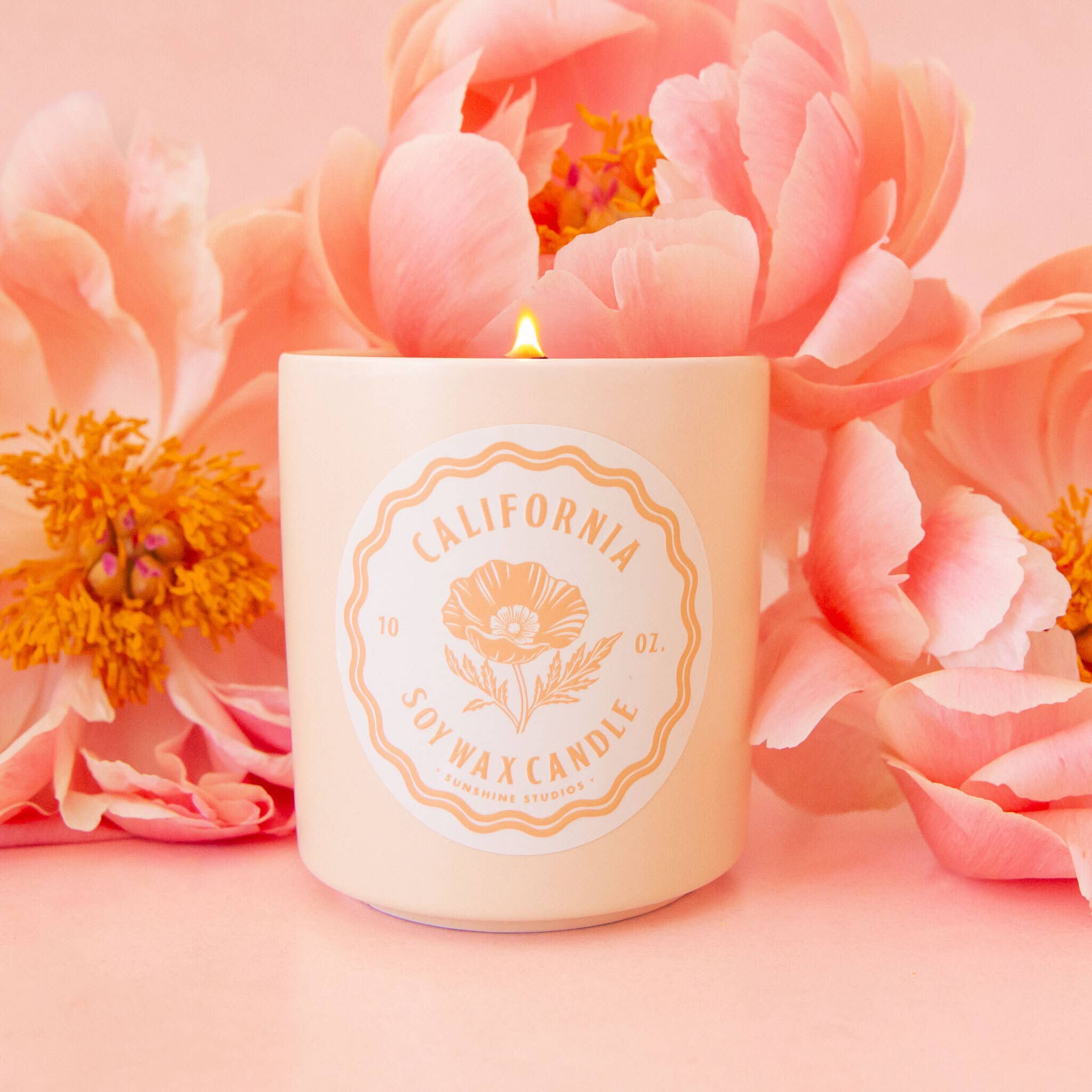 Candle with 'California Soy Wax Candles' label surrounded by pink flowers on a pink background