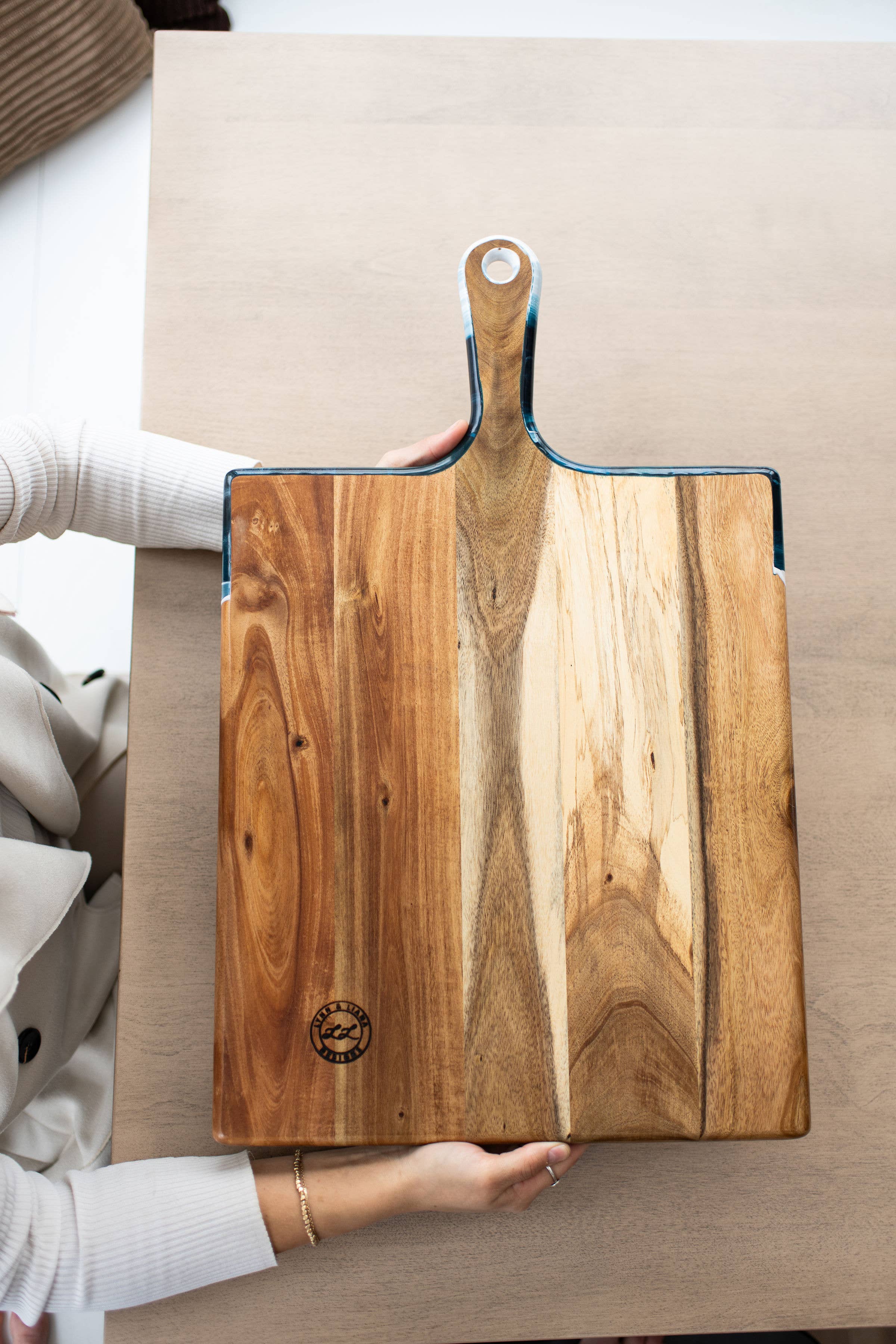 Wooden cutting board with a handle held by a person on a neutral background