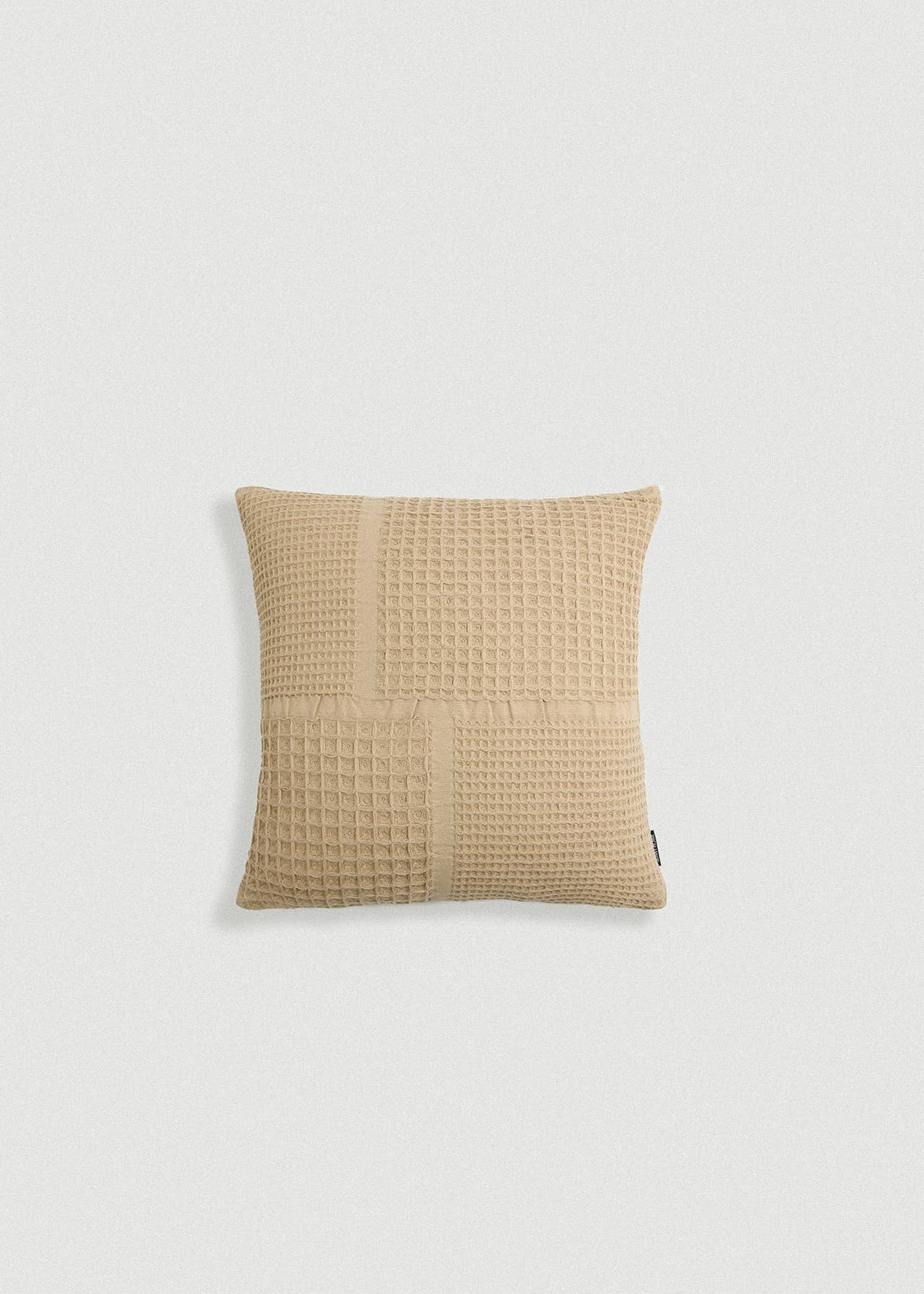 A square beige throw pillow with a textured waffle-weave patchwork design, shown against a plain light gray background.