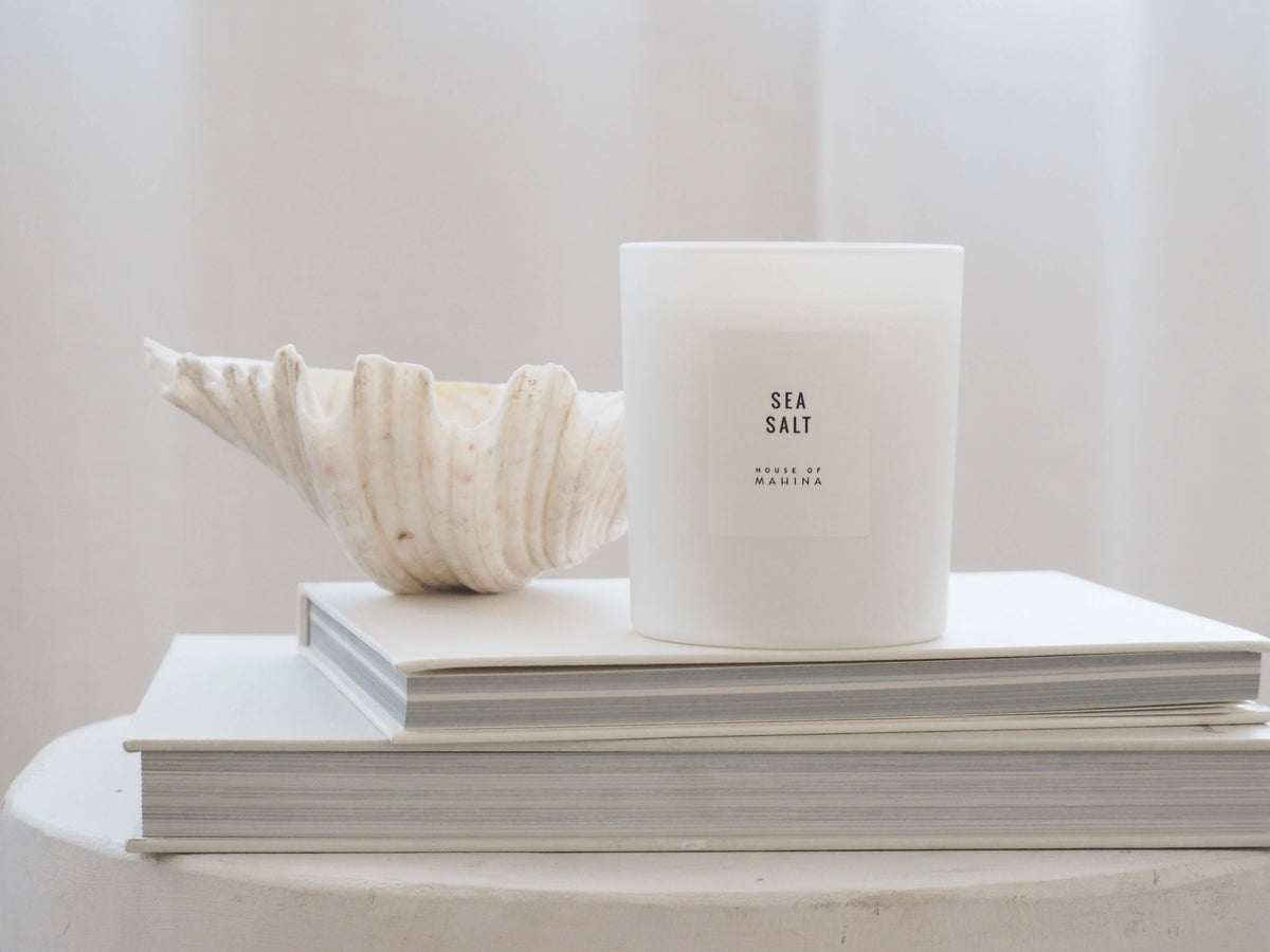 Candle labeled 'Sea Salt' on top of books with a shell beside it against a light background