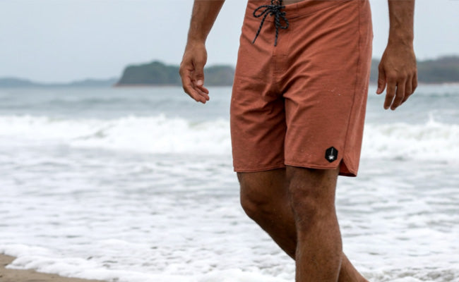Person wearing coral shorts walking on a beach with ocean waves in the background