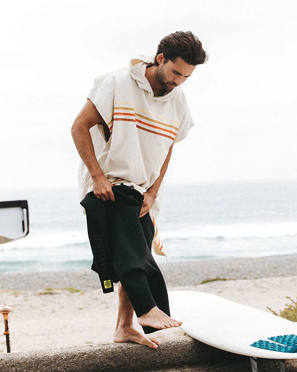 Man on a beach wearing achanging with a Natural Sand Cloud Border Classic Stripe Poncho 