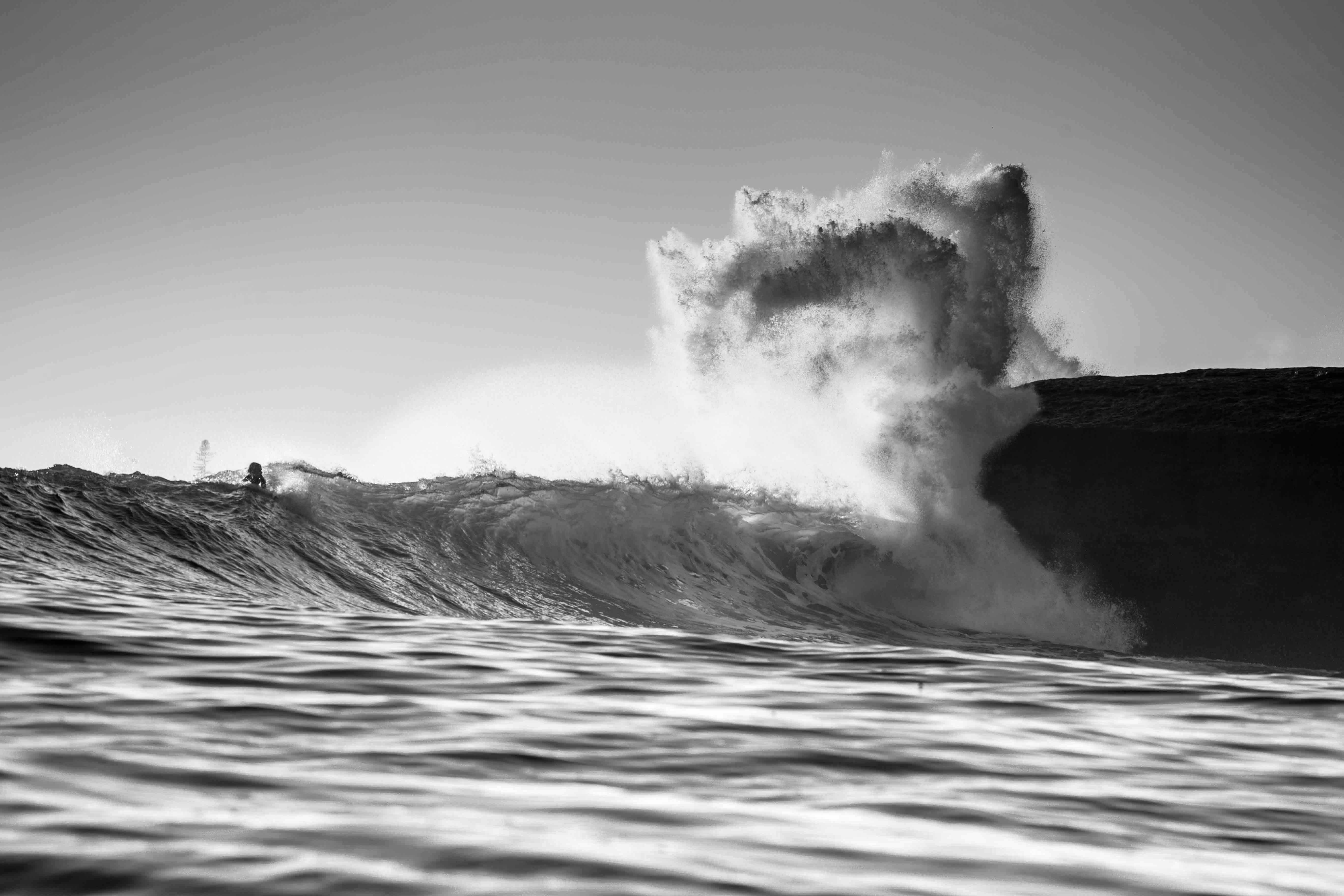 Black and white photo of a large wave crashing with a surfer underneath.